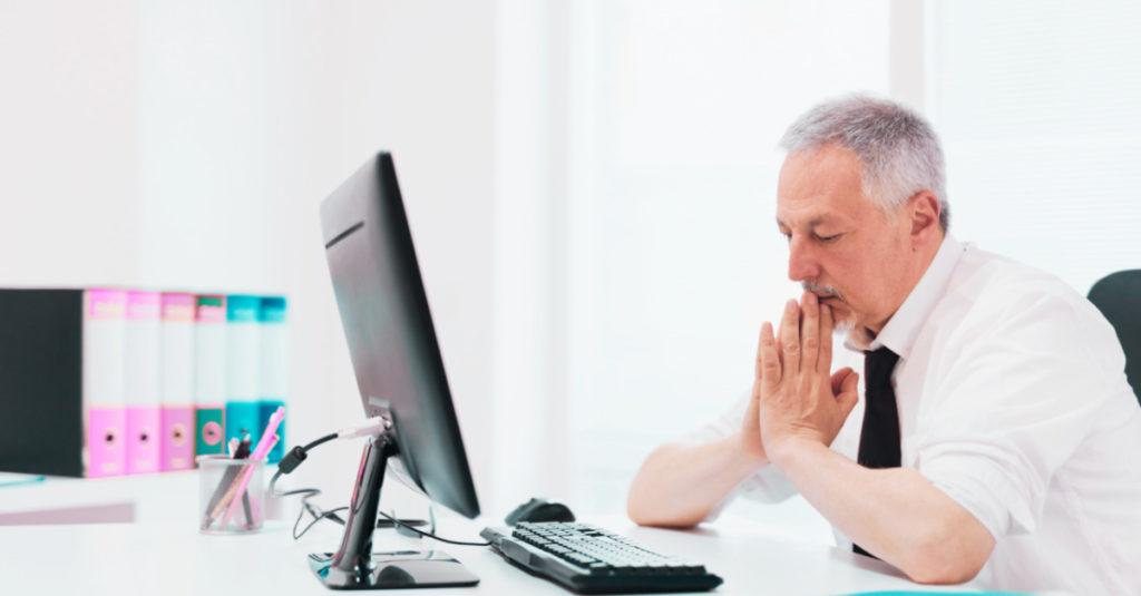 Homem com expressão preocupada diante de um computador. Ele está em um ambiente profissional e representa os gestores preocupados em gerir da melhor forma os pedidos de férias da equipe