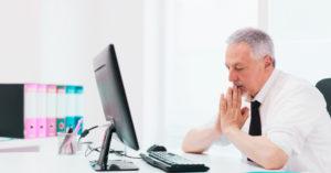 Homem com expressão preocupada diante de um computador. Ele está em um ambiente profissional e representa os gestores preocupados em gerir da melhor forma os pedidos de férias da equipe